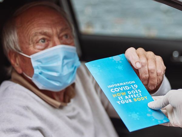 covid vaccination programme man holding covid leaflet that reads 'information covid-19 how does it affect your body'